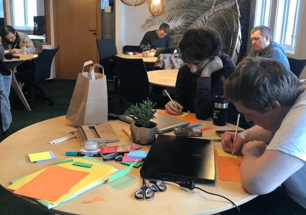 Studenter på Kodehode som sitter rundt et bord og jobber med et gruppeprosjekt