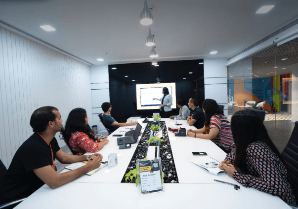 stockfoto av en gruppe mennesker som sitter rundt et bord mens noen presenterer på storskjerm
