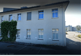 Lang hvit bygning med to etasjer og noe planter som vokser oppover veggen