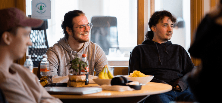 En gruppe studenter på Kodehode som sitter smilende rundt et bord og følger med på undervisning