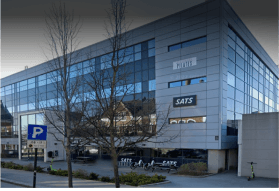 Stor, firkantet, grå bygning med mye vinduer som dekker mesteparten av fasaden, skilt for SATS og Stavanger Pilates på hjørnet i høyre ende.